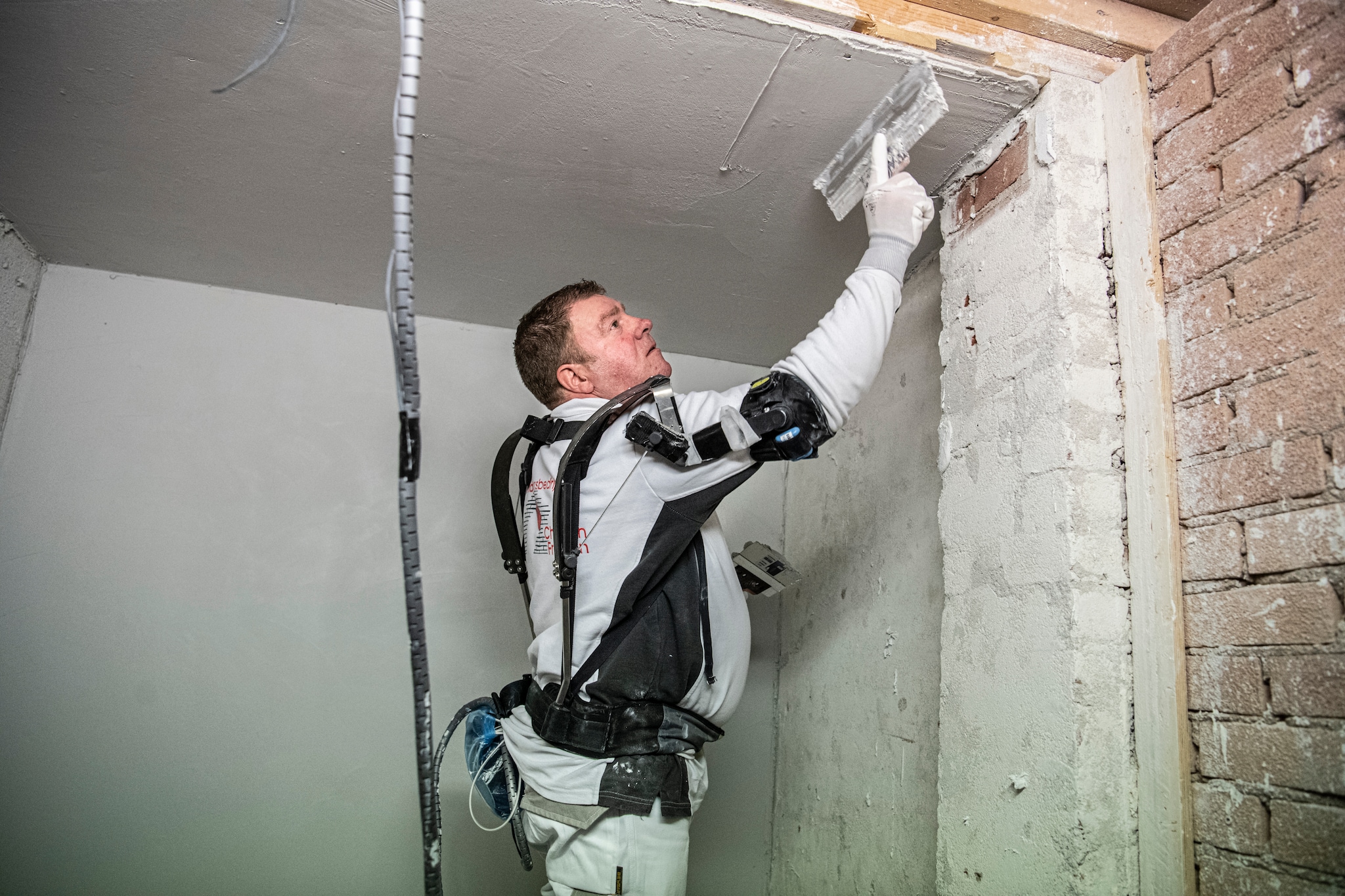 Een stukadoor aan het werk met een exoskelet. Een speciaal verenstelsel genereert kracht die via armsteunen aan hem wordt doorgegeven. Koen Verheijden