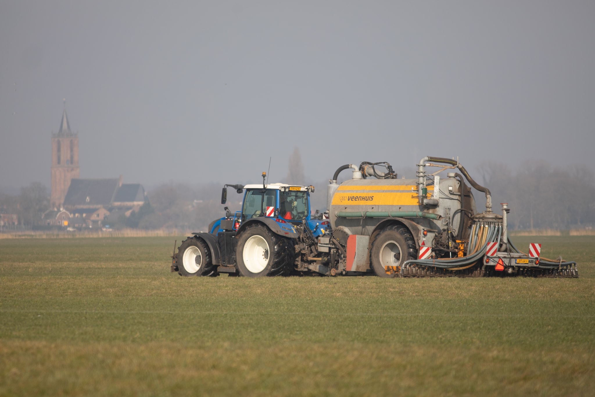Bemesting in de Eempolder.Een tractor met giertank, bemest een perceel grasland in de Zuidpolder van Eemnes.Op de achtergrond de Grote of Sint-Nicolaaskerk in Eemnes. ‘Kunnen we in 2040 nog ons welvaarts- en welzijnsniveau vasthouden als landbouw tweederde van het land in gebruik heeft? Ik denk het niet’, stelt Baarsma. Op de foto bemesting in de Eempolder. Foto: AD/Caspar Huurdeman.