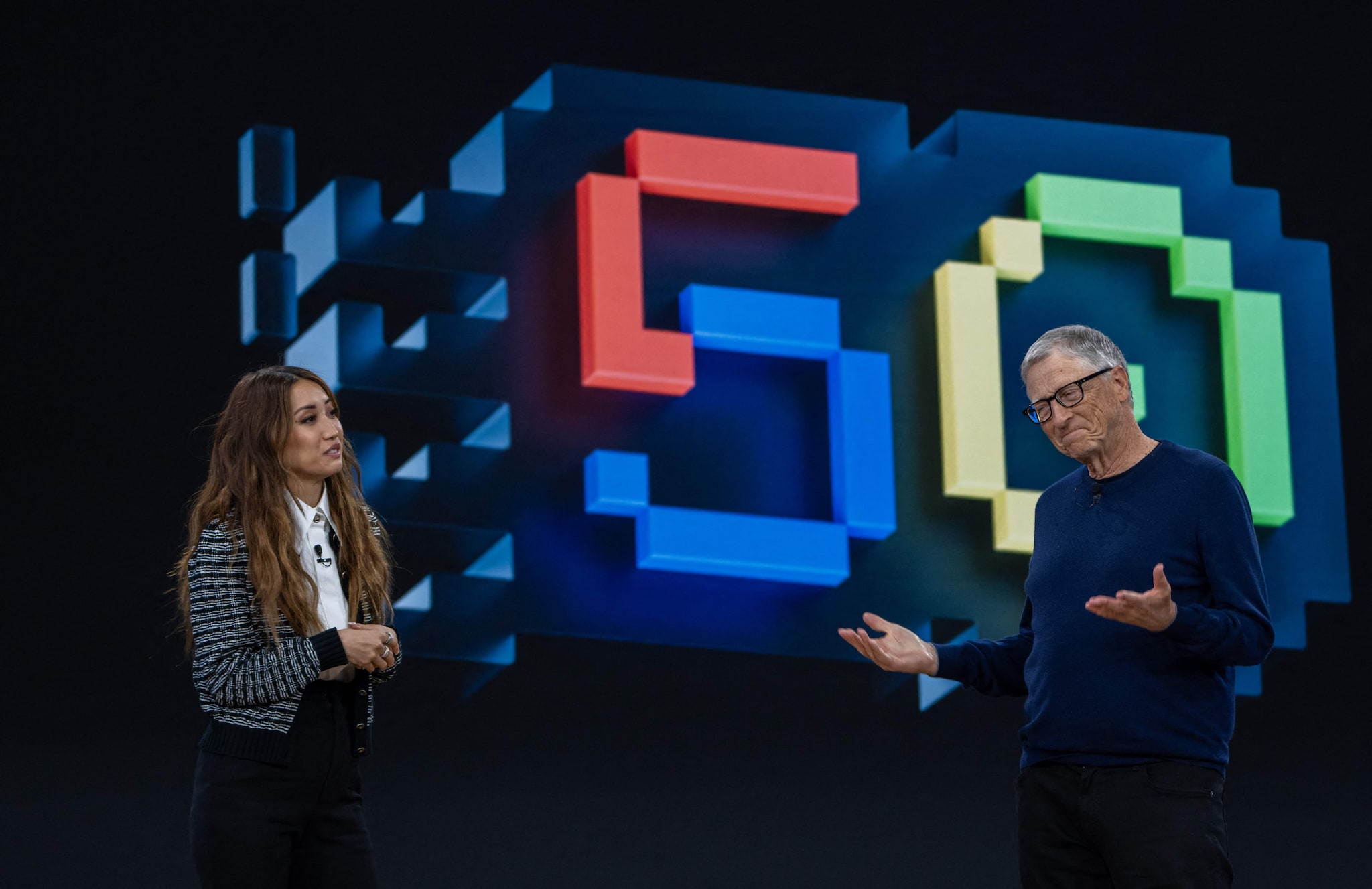 REDMOND, WASHINGTON - APRIL 4: Former Microsoft CEO Bill Gates, right, chats with actor Brenda Song during an event celebrating the 50th Anniversary of the Microsoft April 4, 2025 in Redmond, Washington. The company also gave an update on Copilot, its AI tool.   Stephen Brashear/Getty Images/AFP (Photo by STEPHEN BRASHEAR / GETTY IMAGES NORTH AMERICA / Getty Images via AFP) Bill Gates tijdens het jubileumfeest van Microsoft, met presentatrice Brenda Song, op het podium. Foto: Getty Images via AFP.