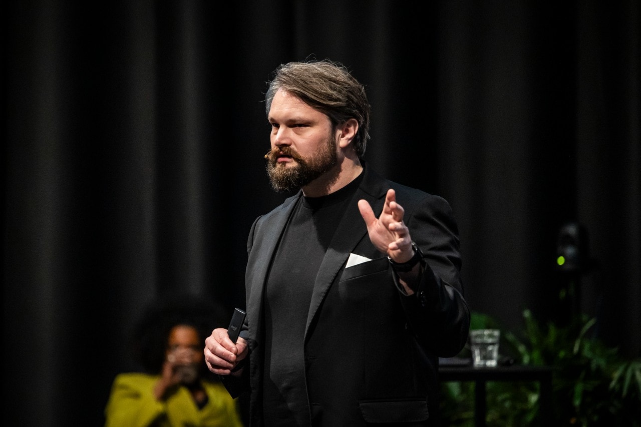 Aragorn Meulendijks op het podium tijdens de Masterclass AI voor Businessleaders in Mediavaert. Toekomst-historicus Aragorn Meulendijks: ‘De slimste mensen ter wereld geven vrijwillig hun privacy op, niet uit luiheid of onwetendheid, maar omdat het competitieve voordeel zo overweldigend is dat ze simpelweg niet anders kúnnen’. Foto: Dingena Mol.