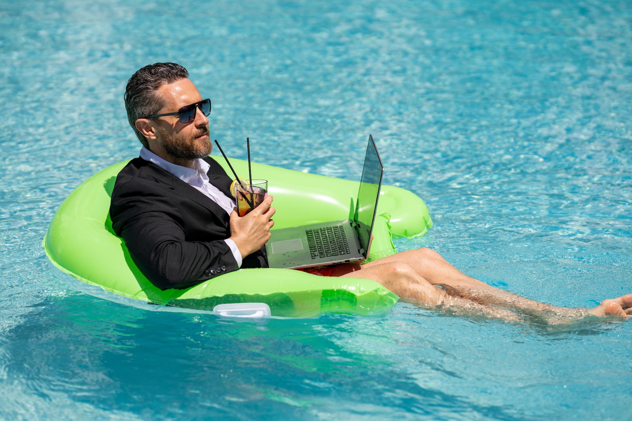 Business man relaxing in suit on swimming pool. Summer vacation, business on sea beach. Terugkeren na de zomervakantie: hoe doe je dat? Foto: Volodymyr TVERDOKHLIB/Shutterstock