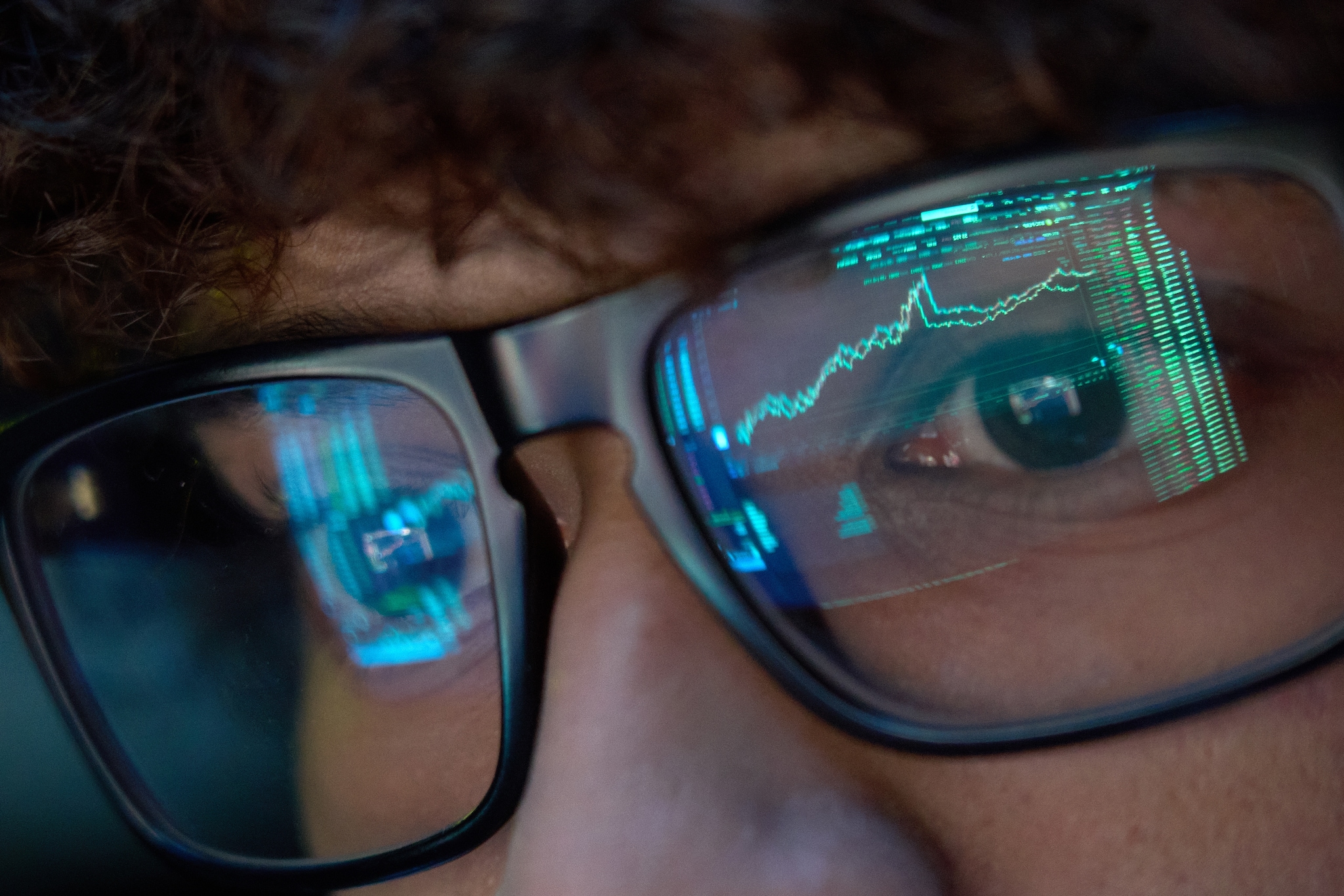 Young business man wearing glasses looking at computer screen with trading charts reflecting in eyeglasses. Inzichten met Agentic Analytics. Foto: Ground Picture/Shutterstock.
