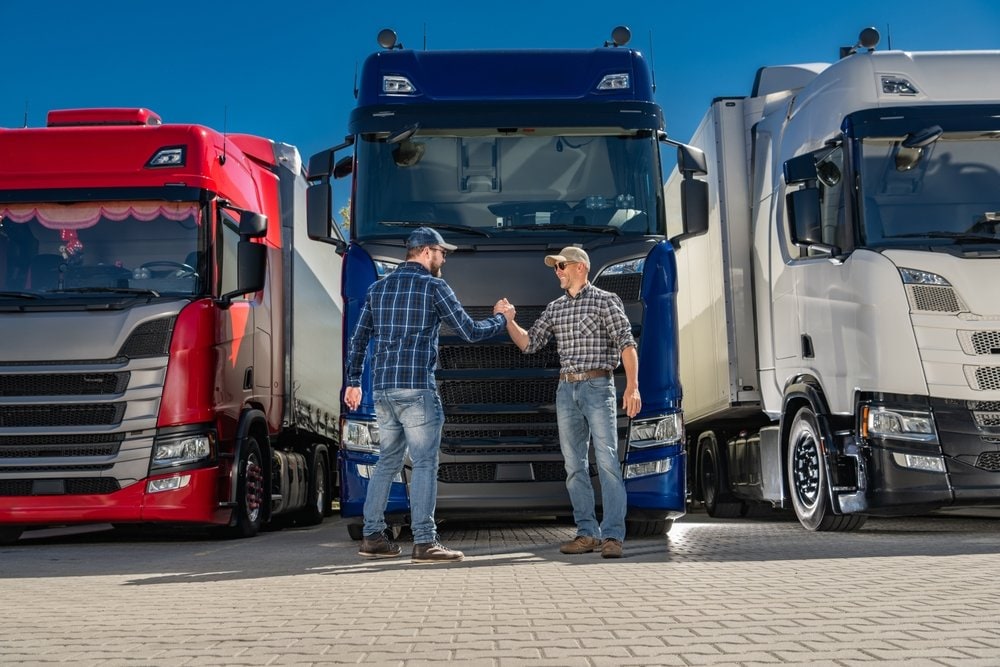 Two caucasian semi truck drivers shaking hands in front of a group of euro trucks. Ook chauffeurs/bestuurders van trucks, industriële heftrucks en tractoren hoeven zich wat AI betreft geen zorgen te maken, blijkt uit onderzoek. Foto: Shutterstock.