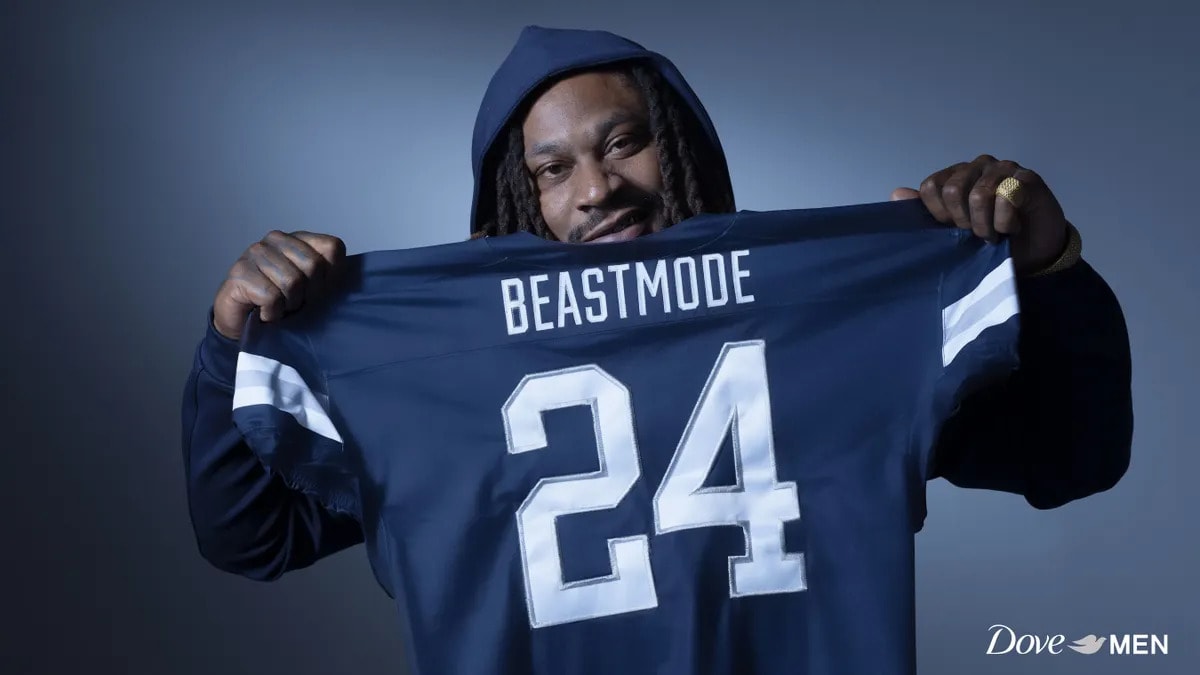 Dove Men+Care-ambassadeur Marshawn Lynch houdt een shirt omhoog met zijn bekende “Beastmode”-slagzin. De atleet speelt een rol in een nieuwe campagne ter promotie van Dove’s sponsoring van het FIFA Wereldkampioenschap 2026. Dove Men+Care-ambassadeur Marshawn Lynch houdt een shirt omhoog met zijn bekende “Beastmode”-slagzin. De atleet speelt een rol in een nieuwe campagne ter promotie van Dove’s sponsoring van het WK voetbal 2026. Foto: Dove Men+Care