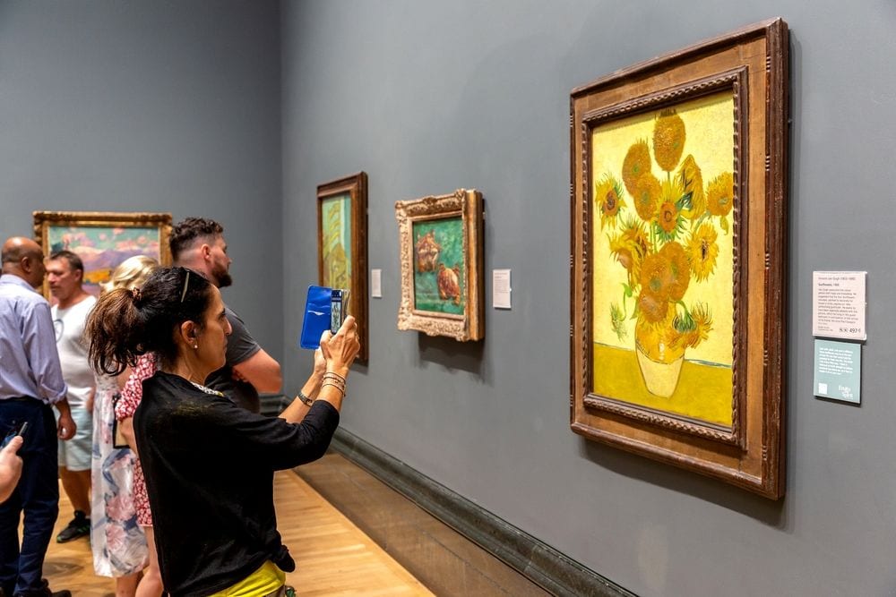 Mensen die naar de olieverfschilderijen "SUNFLOWERS" van Vincent van Gogh kijken in The National Gallery in Londen. Mensen die naar de zonnebloemen-olieverfschilderijen van Vincent van Gogh kijken in The National Gallery in Londen. Foto: Shutterstock.