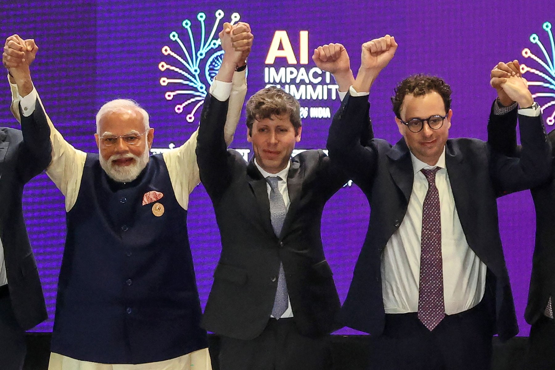 De Indiase premier Narendra Modi (L) gaat op de groepsfoto met kopstukken uit de AI-sector, waaronder OpenAI-CEO Sam Altman (M) and Anthropic-CEO Dario Amodei (R) tijdens de AI Impact Summit in New Delhi op 19 februari 2026. De Indiase premier Narendra Modi (links) met OpenAI-CEO Sam Altman en Anthropic-CEO Dario Amodei tijdens de AI Impact Summit 2026 in New Delhi.