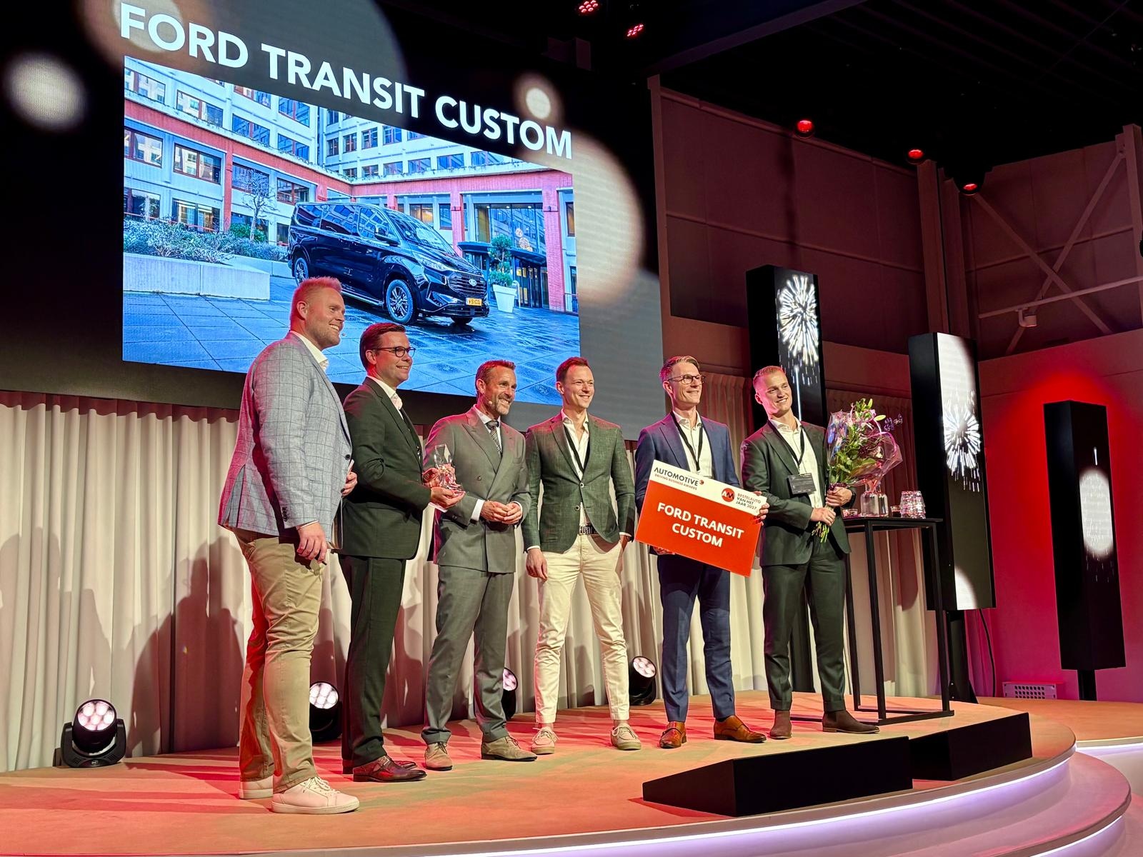 Het trotse team achter Ford Nederland, met hun Transit Custom als Bestelauto van het Jaar 2027. Links awardshow-presentator Roland Tameling. Automotive Online
