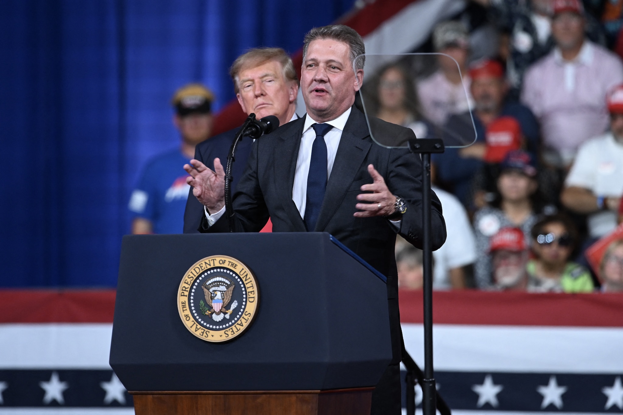 Donald Trump kijkt toe terwijl Audi-topman Gernot Döllner spreekt tijdens een campagnebijeenkomst in Georgia.